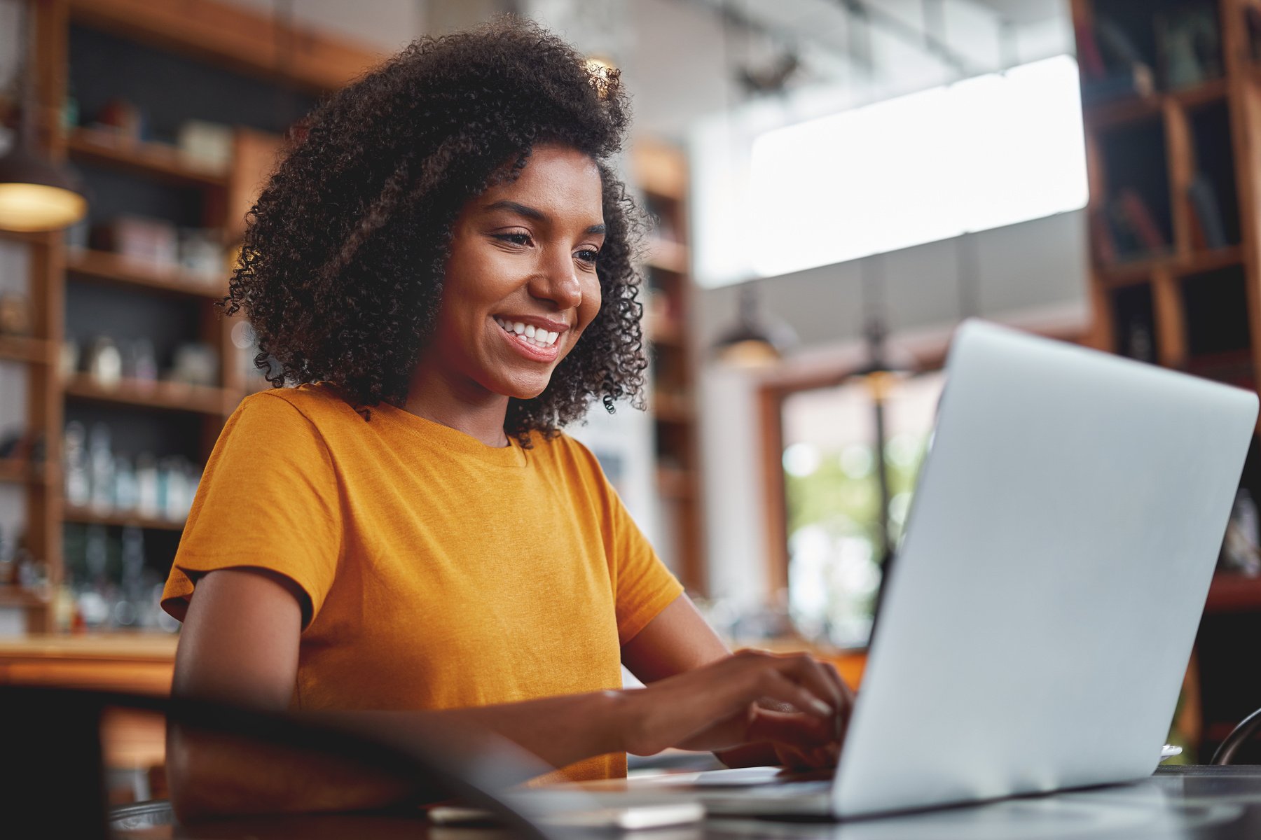 Happy young black woman using laptop in cafe